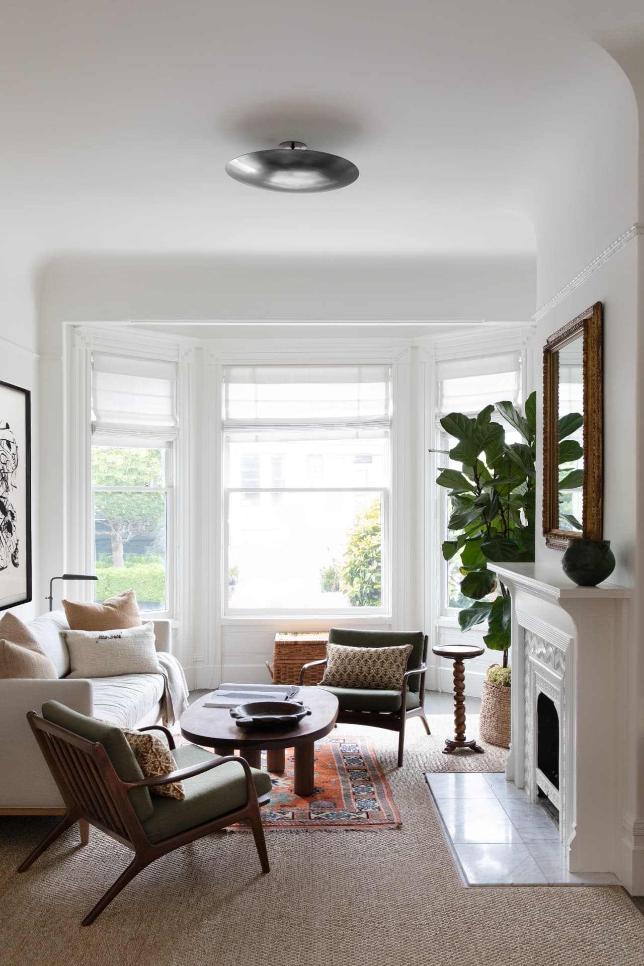 A bright, layered living room with bay windows, vintage furniture, and a marble fireplace